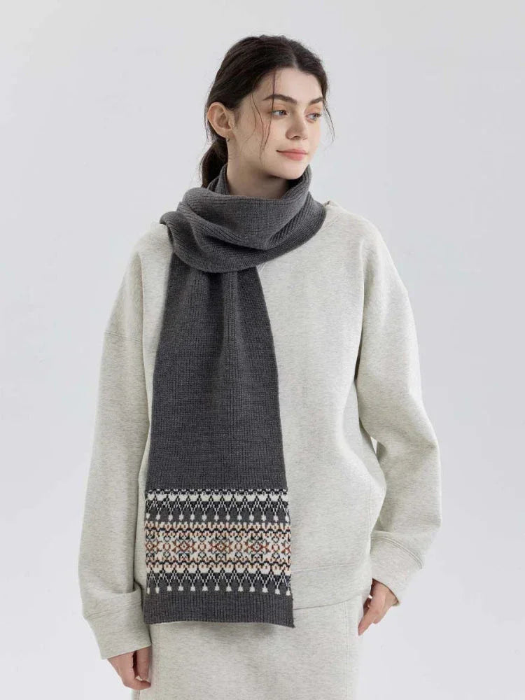 Woman wearing a grey knit scarf with a Fair Isle pattern on the ends, over a grey sweatshirt and matching pants.