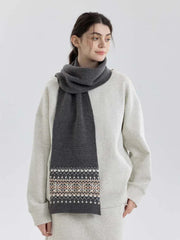 Woman wearing a grey knit scarf with a Fair Isle pattern on the ends, over a grey sweatshirt and matching pants.