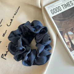 Denim scrunchie on a beige cloth next to a newspaper