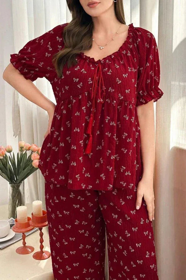 Woman wearing a red pajama set with a butterfly print, standing, with a vase of flowers in the background.