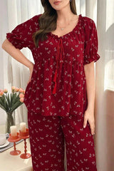 Woman wearing a red pajama set with a butterfly print, standing, with a vase of flowers in the background.