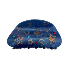 A blue claw hair clip with a celestial pattern of gold stars and moons, accented with colorful gemstones.