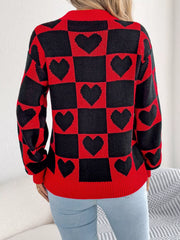 Back view of a woman wearing a red and black checkerboard heart print knitted sweater with light blue jeans