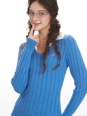 Close-up of a woman wearing a blue cable knit V-neck sweater with a white collar, showing embroidered detail on the chest, front view.