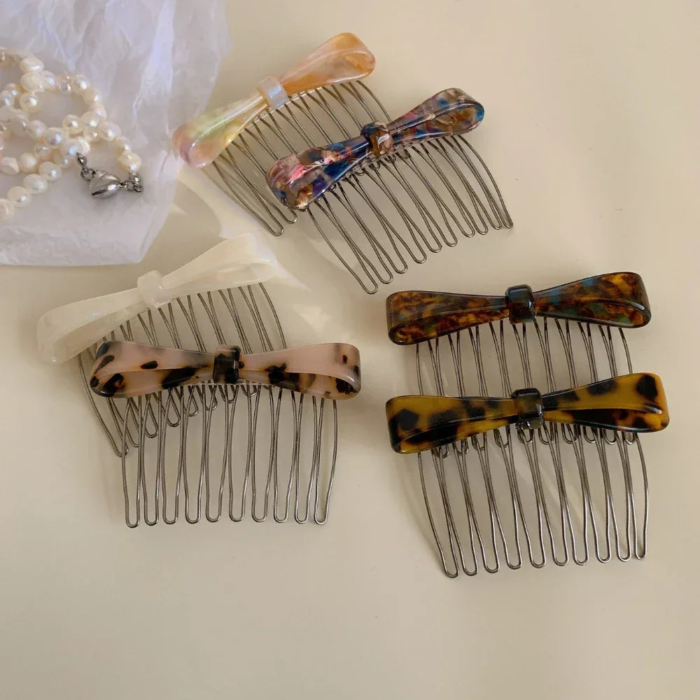 Multiple bow combs are arranged in a grouping on a white surface, with a pearl necklace visible in the background.