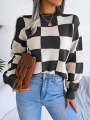 Woman wearing a black and white checkerboard knit sweater with light wash jeans and a brown fringe clutch, front view.