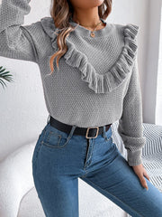 woman wearing a grey knit sweater with ruffle trim, blue jeans, and a black belt striking a pose