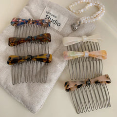 A collection of bow combs with different patterns are displayed on a beige fabric.