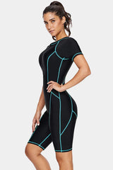 Woman wearing a black short-sleeve one-piece swimsuit with blue contrast stitching, angled side view