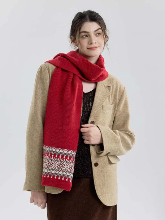 Woman wearing a red knit scarf with a Fair Isle pattern on the ends, over a tan blazer and brown dress.