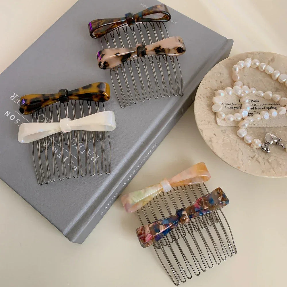 Several bow combs are arranged on a book and next to a pearl necklace.