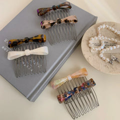 Several bow combs are arranged on a book and next to a pearl necklace.