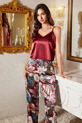 Woman wearing a burgundy satin camisole and floral print satin pants, standing by a vanity.