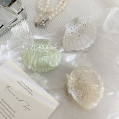 decorative seashell hair clips with rhinestones and glitter arranged with a pearl necklace and card