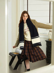 Woman wearing a navy and white striped knit scarf with a tan blazer and plaid skirt
