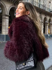 Woman wearing a burgundy shaggy faux fur cropped jacket and a black quilted handbag.