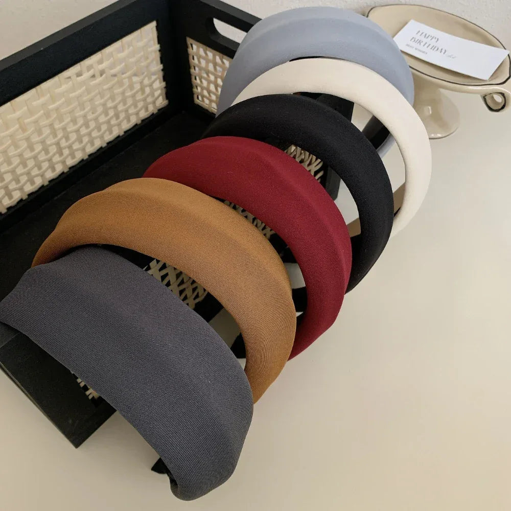 Selection of padded headbands arranged in a basket and on a surface, featuring colors like grey, brown, red, black, cream, and light blue