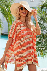 Woman wearing an orange and beige striped crocheted poncho with a V-neck and short sleeves, accessorized with a straw hat and sunglasses.