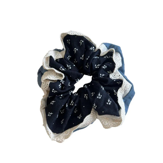 A dark blue scrunchie with a white floral print and white lace trim is shown on a white background.