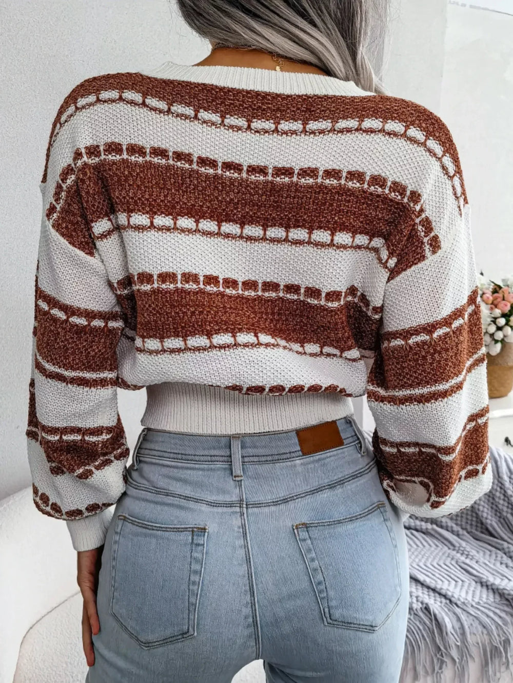 Back view of a woman wearing a brown and white striped cropped knit sweater and light wash jeans.