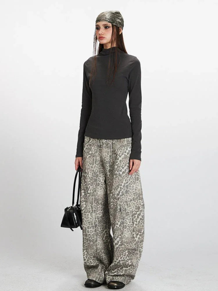Full body shot of a woman in a grey turtleneck top, leopard print pants, and a headscarf.