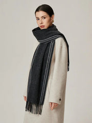 Woman wearing a charcoal gray scarf with white stripes and a cream coat