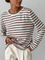 Woman wearing a brown and white striped long-sleeved crew neck sweater with cream-colored pants, hands tucked into her pockets.