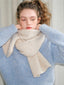 Model adjusting a light blue knit sweater and a cream scarf.