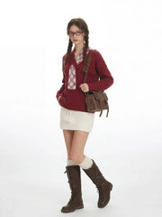 Woman poses with one leg forward, wearing a burgundy v-neck sweater with a white plaid detail, a white textured mini skirt, white knee-high socks, and brown buckled boots, carrying a brown crossbody bag.