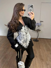 Woman in a black blazer with a white lace corset detail, black leggings, and black boots, holding a white handbag and sunglasses.