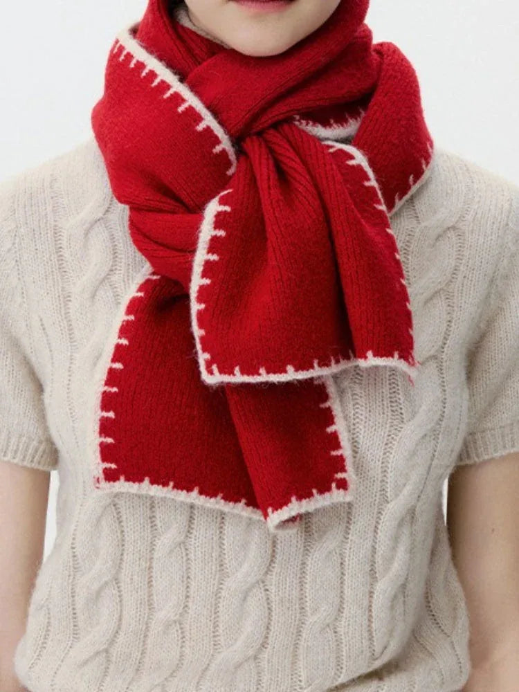 Close-up of a woman wearing a red knit scarf with white contrast stitching over a cream cable knit sweater.
