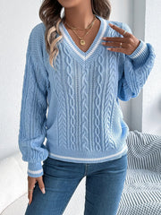 woman adjusting her light blue cable knit v-neck sweater with white stripes, wearing blue jeans and gold rings