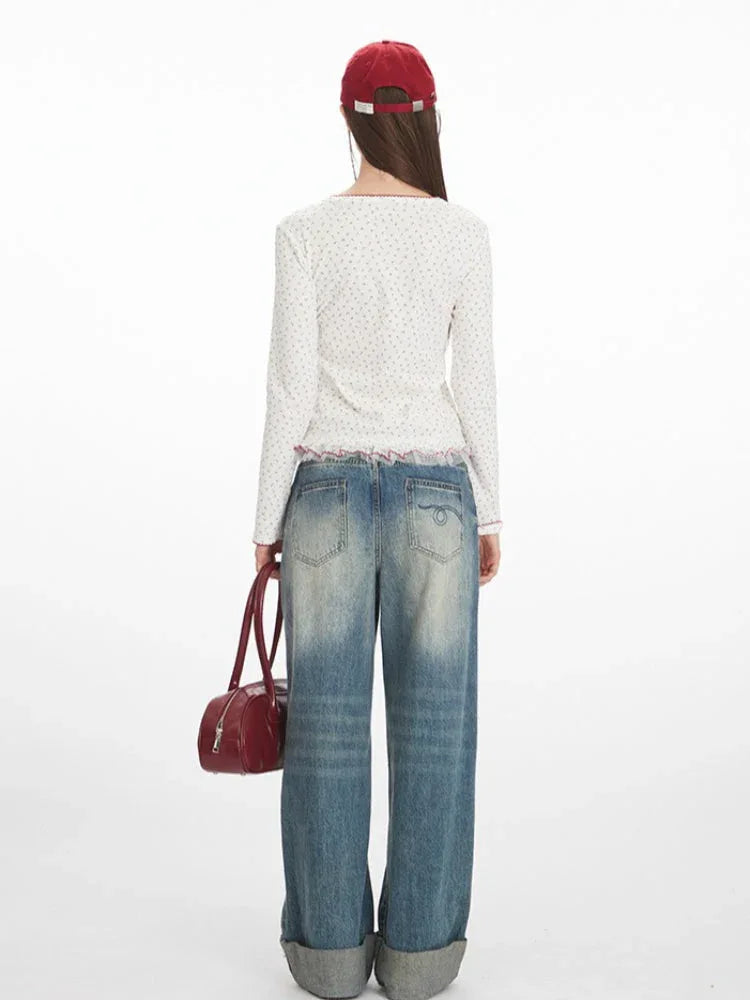 Back view of a model wearing a white long-sleeve top with a floral print and red trim, paired with blue jeans and a red handbag.