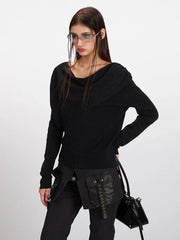 Close-up of a woman wearing a black asymmetrical knit sweater with draped detailing and sunglasses.