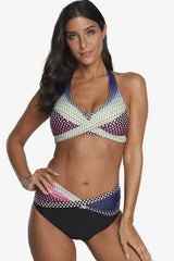 Woman wearing a multi-colored polka dot halter neck bikini with high-waisted black bottoms, front view.