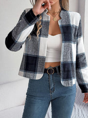 Woman wearing a cropped buffalo plaid jacket over a white tank top and blue jeans, with a black belt, touching her necklace.