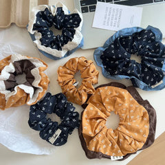 A group of scrunchies, featuring floral prints and decorative edges, are scattered on a white surface near a laptop.