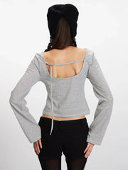 Back view of a model wearing a grey and white striped long-sleeved cropped top with an open back and a tie detail.