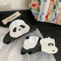 Two panda hair claw clips on a dark surface with a textured bag in the background