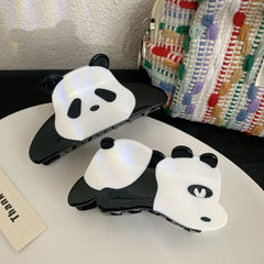 Two panda hair claw clips on a white surface with a textured bag in the background