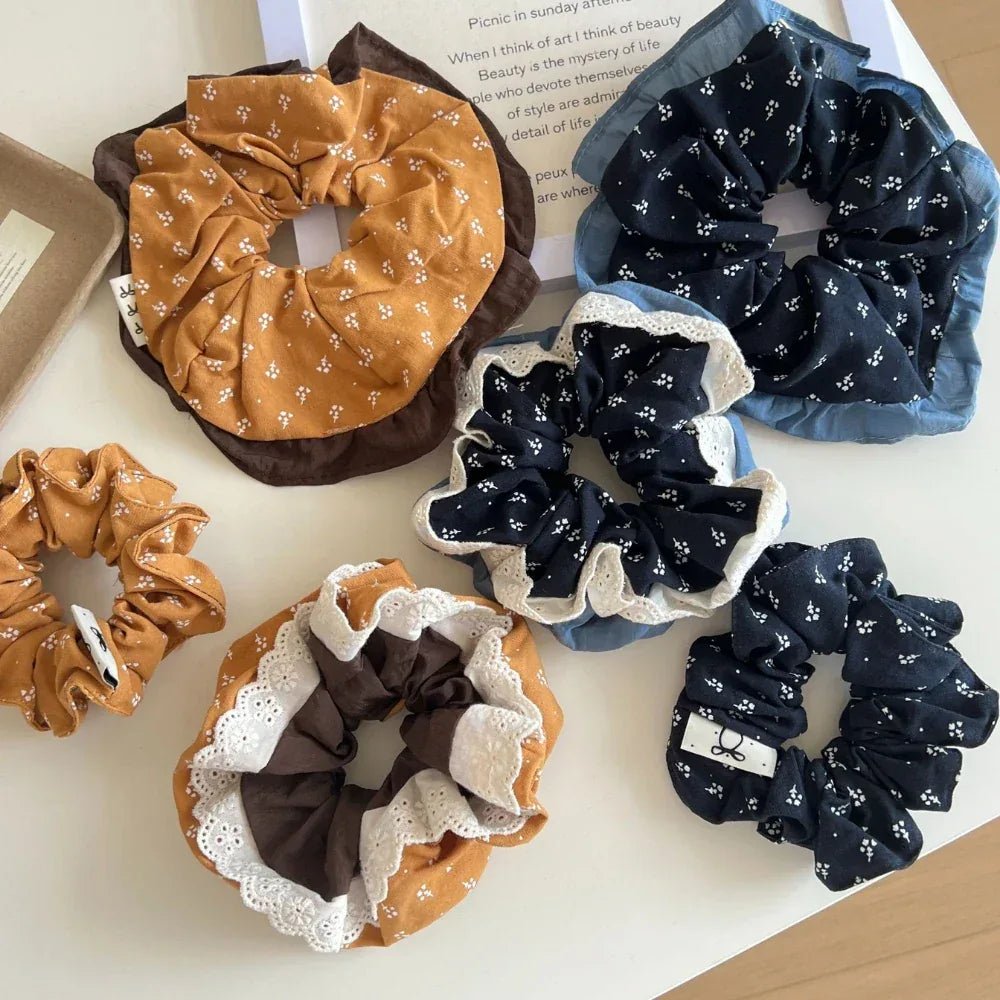 A variety of scrunchies, some with floral patterns and lace detailing, are displayed from a top-down perspective.