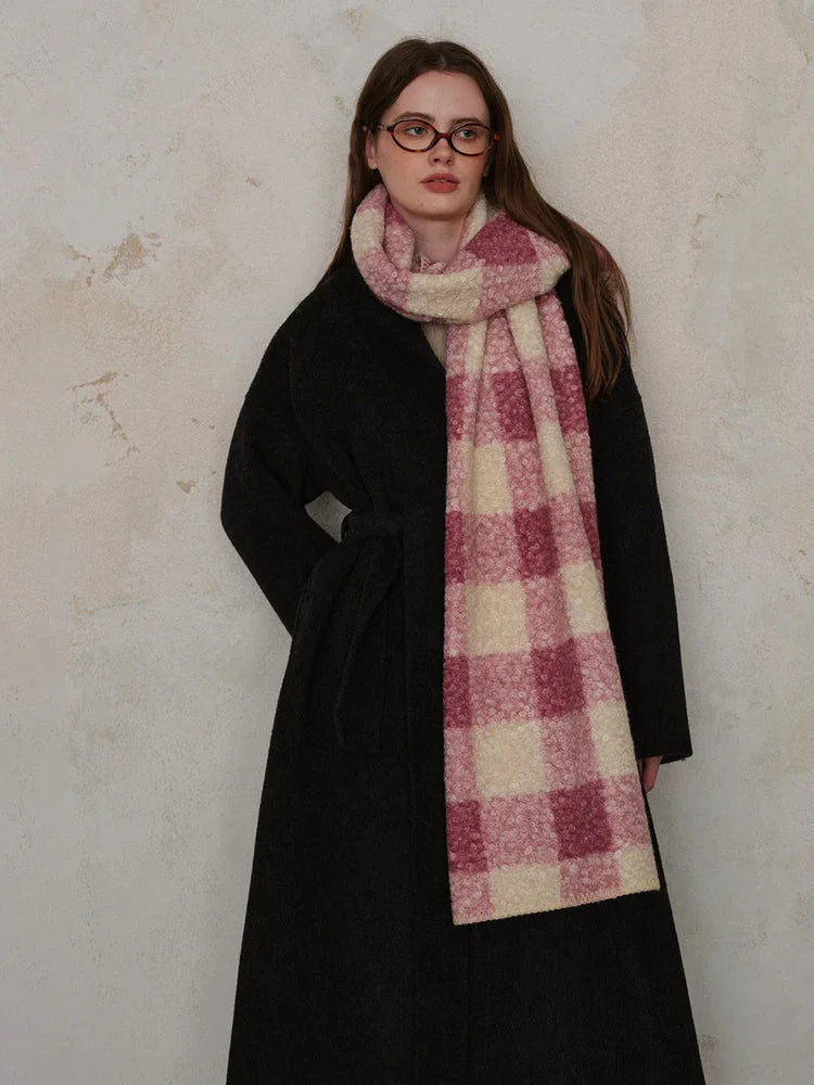 Woman wearing a black coat and a pink and cream plaid scarf, hands in pockets.