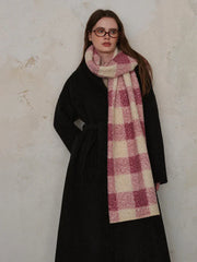 Woman wearing a black coat and a pink and cream plaid scarf, hands in pockets.