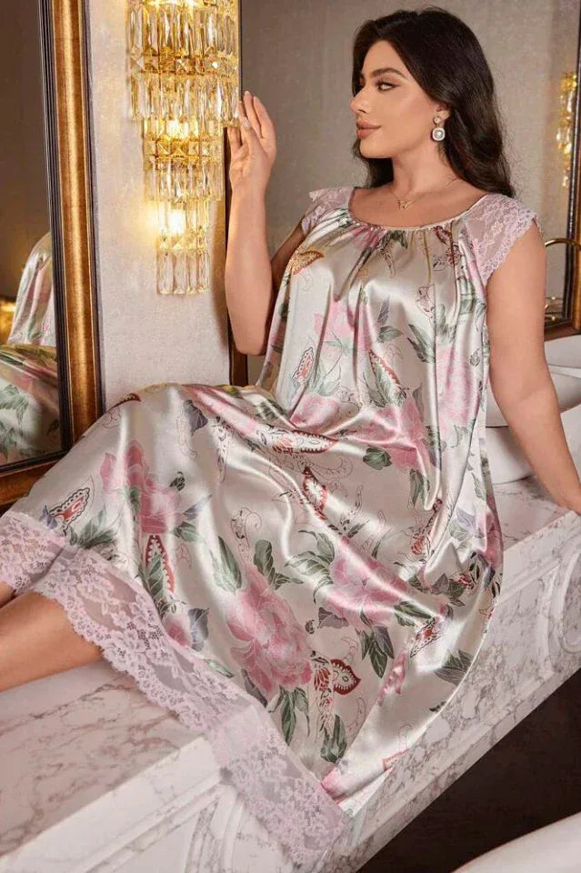 Woman sitting on a surface wearing a floral and butterfly print satin nightgown with lace trim.