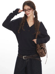 Close-up of a woman wearing a dark long-sleeved V-neck top, adjusting her glasses, with a brown leather crossbody bag, posing against a white background.