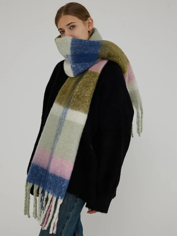 Woman wearing a black sweater and a large plaid scarf with green, pink, blue, and white blocks wrapped around her neck.