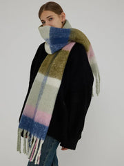 Woman wearing a black sweater and a large plaid scarf with green, pink, blue, and white blocks wrapped around her neck.