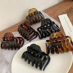 overhead view of six hair claw clips in black and tortoise shell patterns on a white cloth and wooden surface