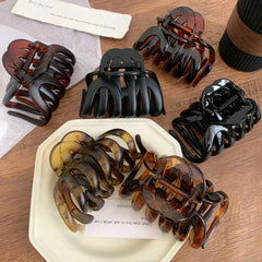 top-down view of five hair claw clips in black and tortoise shell patterns on a white plate and wooden surface