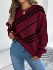 Woman showing the hem of a burgundy knit sweater with black diagonal stripes, blue jeans, and gold rings.